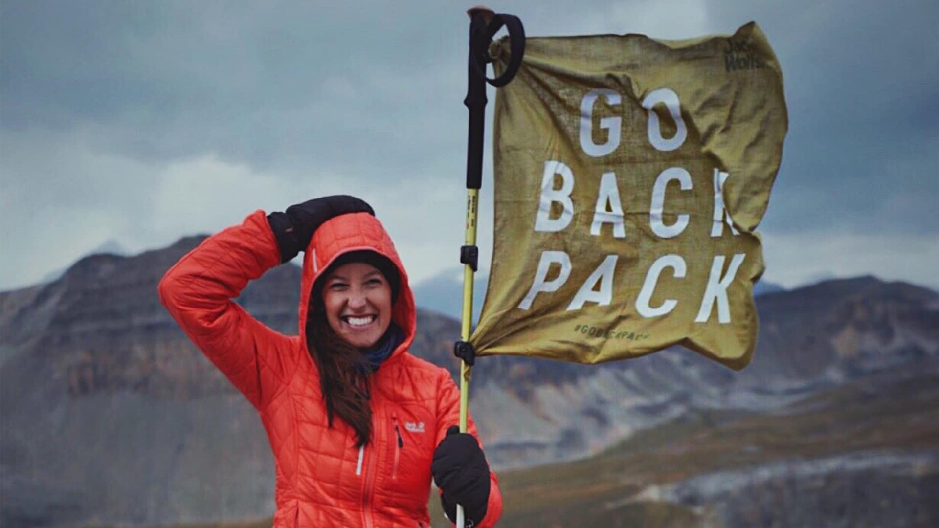Junge Frau hält eine Flagge mit der Aufschrift GO BACK PACK für die Jack Wolfskin Kampagne #GOBACKPACK