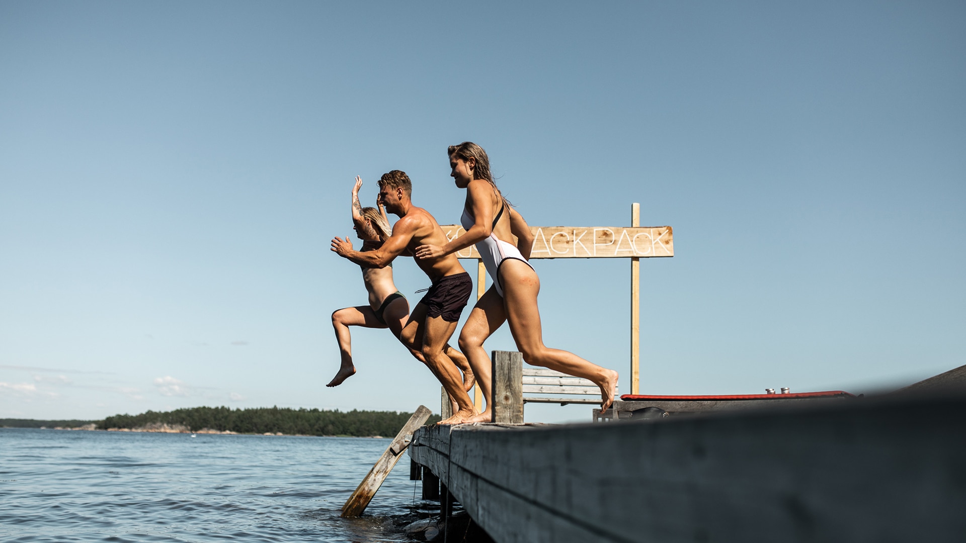Drei junge Leute springen von einem Steg in den See für die Jack Wolfskin Kampagne #GOBACKPACK