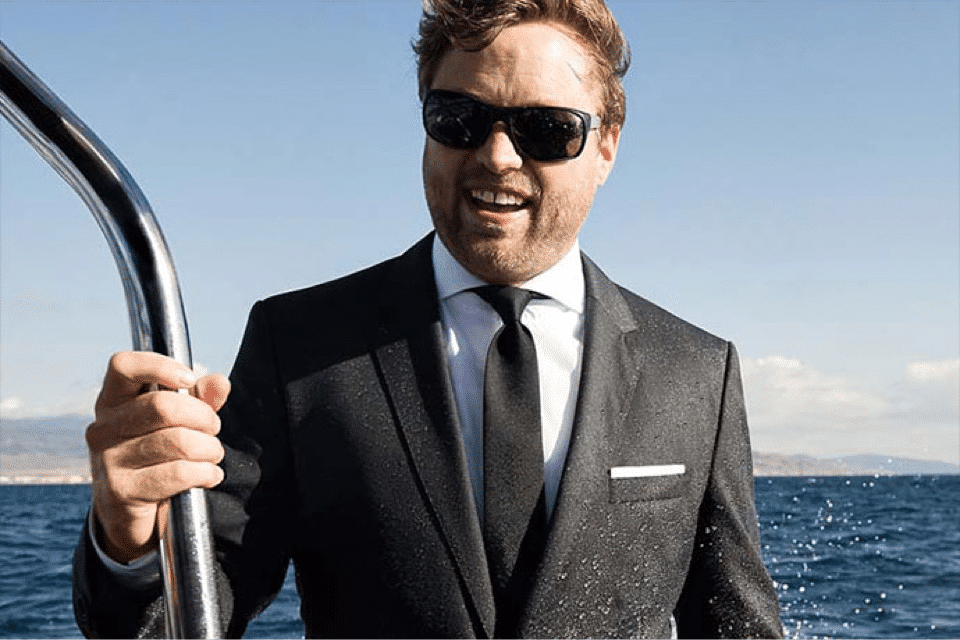 Mann im schwarzen Anzug steht auf einem Segelboot für die Hugo Boss Social Media Kampagne
