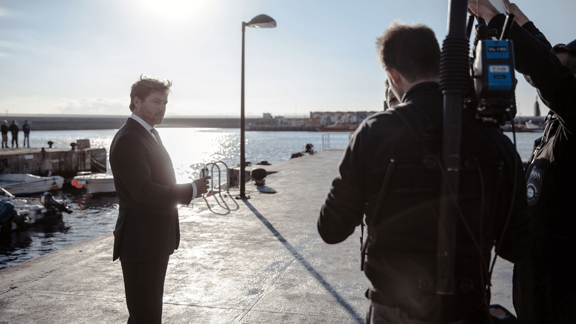 Mann im schwarzen Anzug steht am Hafen, neben ihm ein Kamerateam für die Hugo Boss Social Media Kampagne