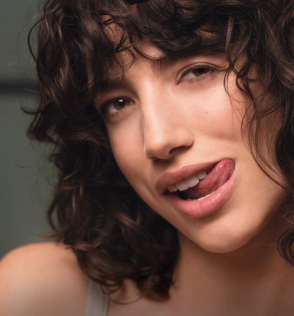 Junge Frau mit braunen Locken streckt die Zunge raus im Rahmen der Bio.Vegane Kampagne