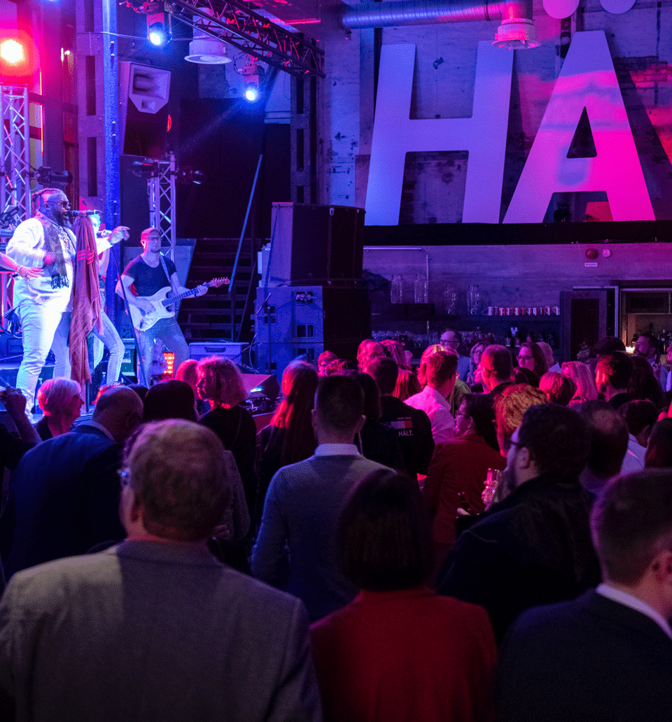 Feiernde Menschen in einer Industrie-Halle, auf der Bühne spielt eine Band für die Hakro Jubiläumsfeier