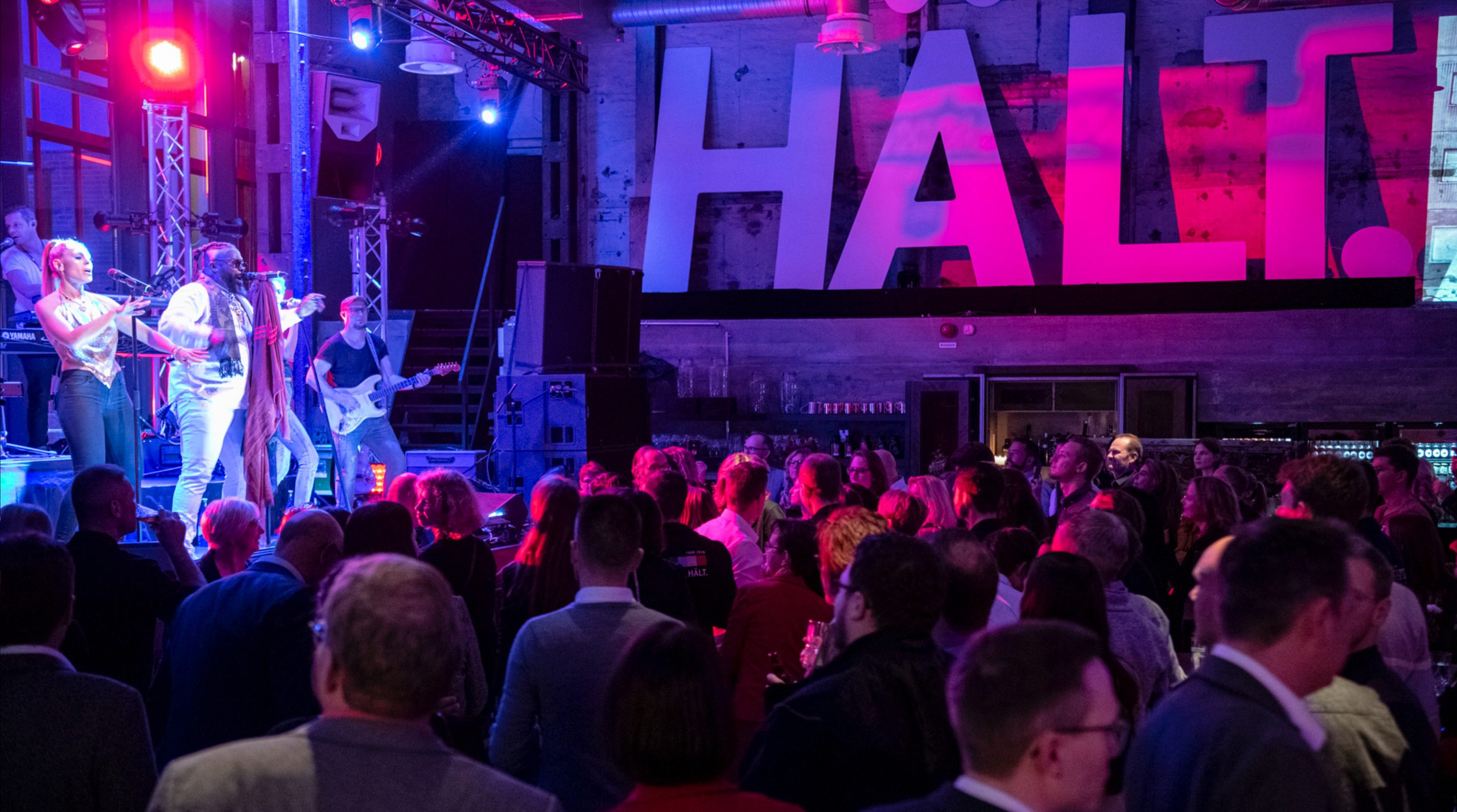 Feiernde Menschen in einer Industrie-Halle, auf der Bühne spielt eine Band für die Hakro Jubiläumsfeier